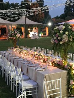 a long table is set up with flowers and candles for an outdoor wedding reception in the evening