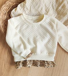 a white sweater sitting on top of a wooden floor next to a straw hat and basket