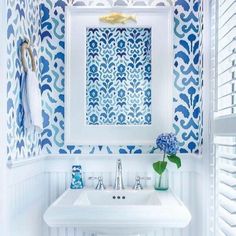 a white sink sitting under a bathroom mirror next to a blue and white wallpaper