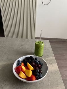 a white bowl filled with fruit next to a green smoothie