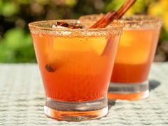 two glasses filled with liquid sitting on top of a table next to each other and cinnamon sticks sticking out of them