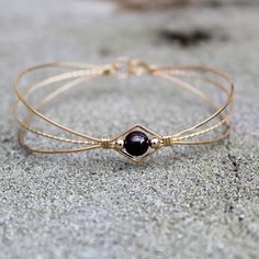 A sweet design of three strands of 14kt gold filled wire featuring a single 6mm genuine garnet bead flanked by two small 14kt gold filled beads. The garnet bead is a very deep dark red, almost black (unless you hold it up to the light or next to something that's actually black!) This stylish, well-fitting bangle will go with most everything in your closet, and is sure to get noticed every time you wear it. So delicate and feminine! The sturdy built-in hook and eye clasp is easy to get on and off Handmade Adjustable Yellow Gold Pearl Bracelet, Gold Double Strand Beaded Bracelet Gift, Gold Double Strand Beaded Bracelet For Gift, Adjustable Handmade Yellow Gold Pearl Bracelet, Gold Wire Wrapped Bracelets With Round Beads, Delicate Adjustable Hand Wrapped Jewelry, Gold Hand-wrapped Bracelets For Gifts, Hand Wrapped Gold Bracelets As Gift, Hand Wrapped Gold Bracelets For Gift