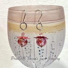 the earrings are decorated with pink glass and silver wire, on top of a white vase