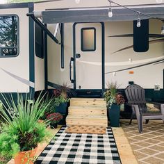 an rv is parked in front of some plants and chairs on the patio with black and white checkered rugs