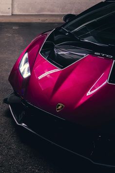 a red sports car parked in a parking lot next to a garage door with the hood up