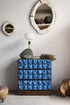 a blue dresser sitting in front of a mirror on top of a white wall next to a wooden stool