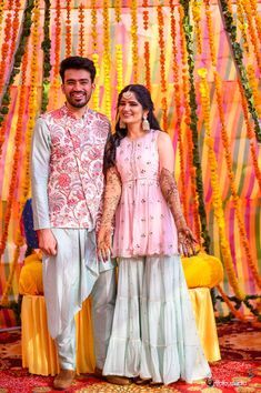 a man and woman standing next to each other in front of a backdrop with flowers