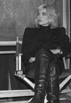 a woman sitting in a chair with her legs crossed and wearing black boots, looking off to the side