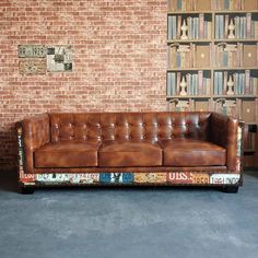 a leather couch sitting in front of a brick wall with bookshelves behind it