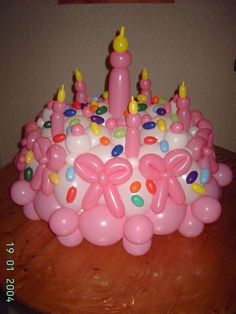 a pink birthday cake with candles and balloons on the top is sitting on a table