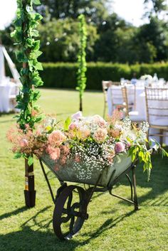 a wheelbarrow filled with flowers sitting on top of a lush green field next to tables