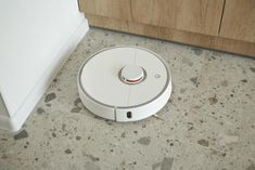 a white robot vacuum on the floor next to a wall and cupboards in a kitchen