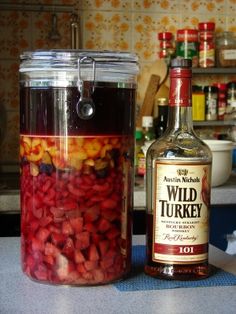 a bottle of alcohol sitting on top of a counter next to a jar filled with fruit