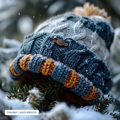 a knitted hat sitting on top of a tree branch covered in snow and pine needles