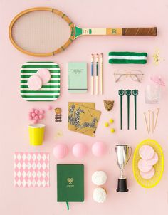 various items are arranged on a pink surface with green and white accessories, including a tennis racquet