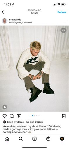 a man sitting on top of a bed next to a white sheet covered wall and wearing black boots