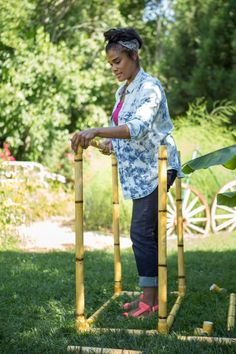 a woman standing next to a wooden structure made out of sticks and bamboo poles in the grass