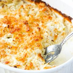 a close up of a casserole in a white dish with a serving spoon