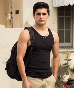 a young man with a backpack standing in front of a white building and looking at the camera