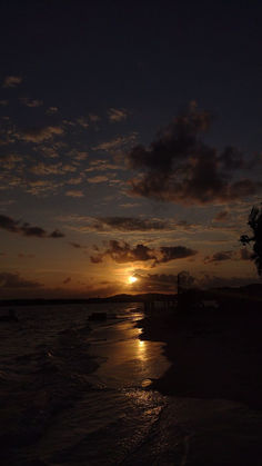 the sun is setting over the ocean with clouds in the sky and some boats on the water