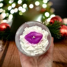 a person holding a wine glass with a purple flower in it and christmas lights behind them