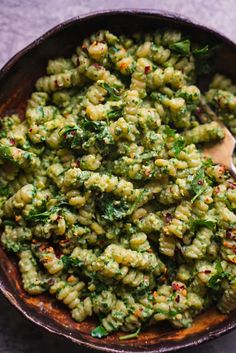 a wooden bowl filled with pasta covered in pesto