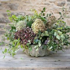 a vase filled with lots of green and purple flowers on top of a wooden table