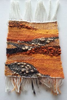 an orange and black piece of cloth with fringes on the bottom, sitting on a white surface