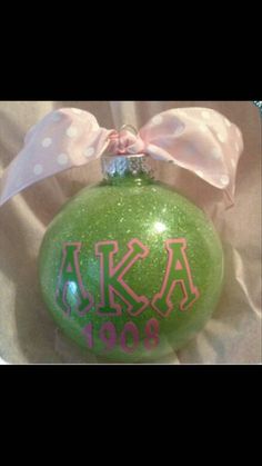 a green ornament with pink letters and a bow on it's side