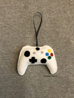 a felt video game controller ornament hanging on a gray t - shirt with black and white buttons