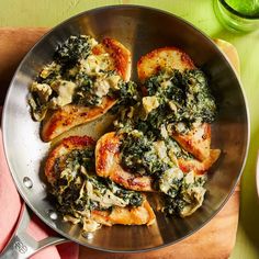 a pan filled with chicken and spinach on top of a wooden cutting board