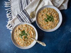 two white bowls filled with soup on top of a blue tablecloth next to silver spoons