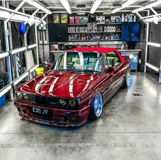 a red car parked in a garage next to some shelves with other items on it