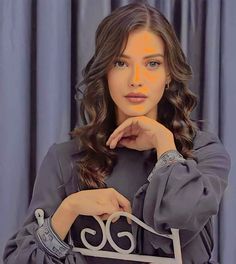 a woman is posing with her hand on her chin and looking at the camera while standing in front of a blue curtain