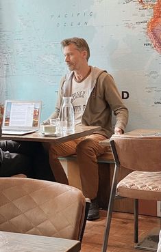 two men sitting at a table in front of a map on the wall behind them