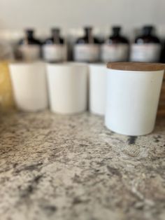 several white cups sitting on top of a counter next to some brown and black bottles