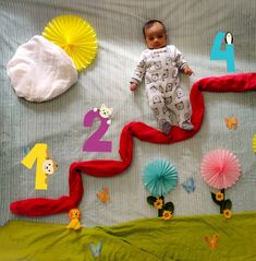 a baby laying on top of a bed next to paper flowers and other items in the shape of numbers