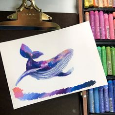 a drawing of a blue whale on paper next to colored crayons