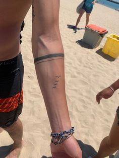 two people standing on the beach with their feet in the sand and one has a tattoo on his arm