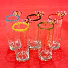 four glasses with rings on them sitting on a red tableclothed surface, one is empty and the other two are filled with water