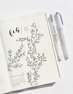 an open notebook with flowers and numbers on the page, next to two marker pens