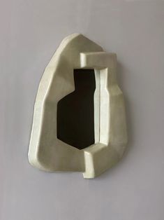 a white sculpture with a black hole in it's center on a gray wall