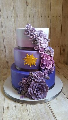 a three tiered cake with purple flowers on the bottom and yellow sun on top