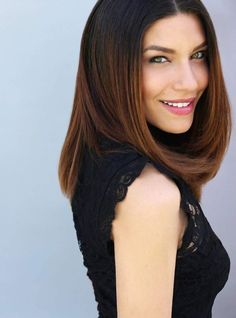 a woman with long brown hair and green eyes smiling at the camera while wearing a black dress