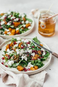 two plates filled with salad next to a jar of honey on a white tablecloth