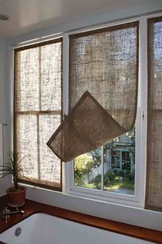 a bath tub sitting under two windows next to a window covered in blinds and a potted plant