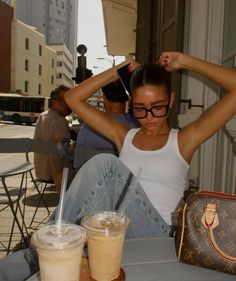 a woman sitting at a table with two cups of coffee and a handbag in front of her