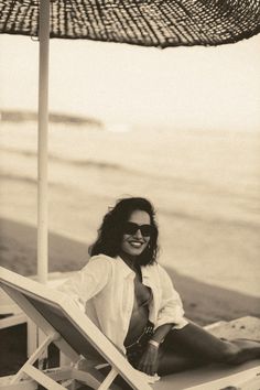 a woman sitting on top of a beach chair under an umbrella