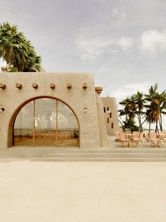 an adobe - style building with palm trees and chairs in front of it, on the beach