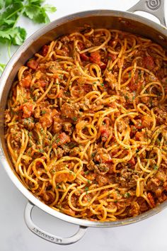 a large pot filled with spaghetti and meat on top of a white tablecloth next to some parsley